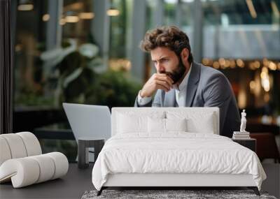 Worried businessman in a hotel lobby, using his laptop to review finances trying to dodge an economic downturn. Concept of concern over the recession Wall mural