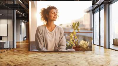 Young woman relishing a moment of peace and reflection on her balcony, emanating gratitude and contentment and enjoying sun rays Wall mural