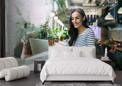 Beautiful happy young woman using laptop and drinking cup of coffee in cafe while lunch time Wall mural