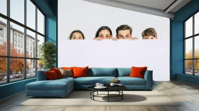 Beautiful smiling family in white T-shirts hold in hands the big blank banner and looking on camera Wall mural