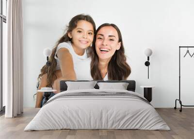 Beautiful young brunette mother holds on back her cute little daughter in white T-shirts isolated in studio Wall mural