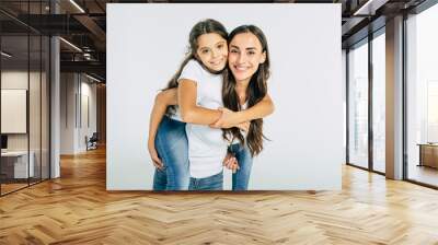 Beautiful young brunette mother holds on back her cute little daughter in white T-shirts isolated in studio Wall mural