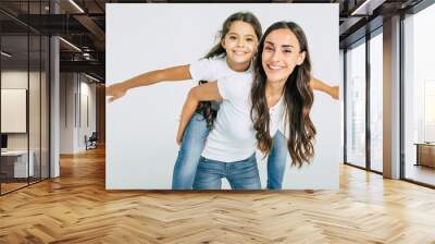 Beautiful young brunette mother holds on back her cute little daughter in white T-shirts isolated in studio Wall mural