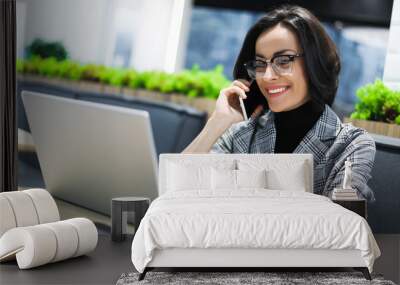 Climbing the career ladder. Close-up photo of a young female office worker talking on the phone with clients and working on her laptop. Wall mural