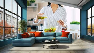 Close up photo of a smiling young woman makes a fresh vegan salad while she uses olive oil for it. Wall mural