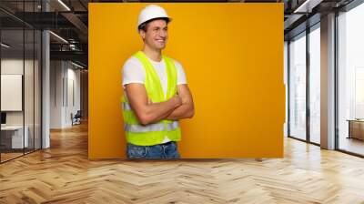 Close up photo of young happy and confident foreman or architect in build helmet is posing isolated on yellow background. Wall mural