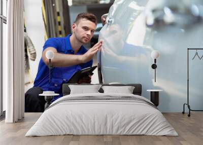 Confident and concentrated young and experienced car repair specialist with a tablet in his hand inspects and diagnosis the car for breakdowns Wall mural