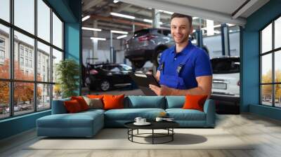 Confident and concentrated young and experienced car repair specialist with a tablet in his hand inspects and diagnosis the car for breakdowns Wall mural