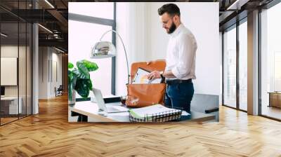 Confident successful bearded businessman in glasses is packing some documents in his office bag at the workplace after job Wall mural