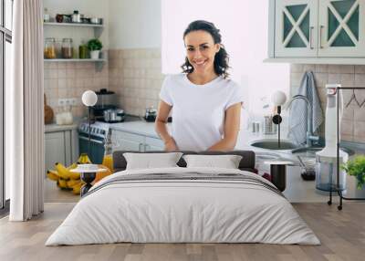 Cute beautiful and happy young brunette woman in the kitchen at home is preparing fruit vegan salad or a healthy smoothie and having fun Wall mural