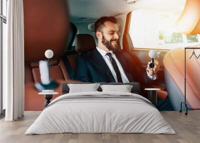 Good news! Handsome smiling business man with mobile phone on hand in car Wall mural