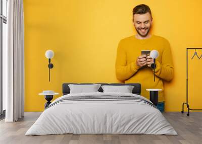 Handsome stylish young beard man in yellow with smart phone in hands is standing over yellow wall Wall mural