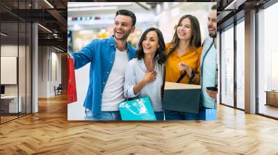 Happy group of excited beautiful modern stylish friends in casual wear with paper bags are walking in the mall during shopping. Wall mural