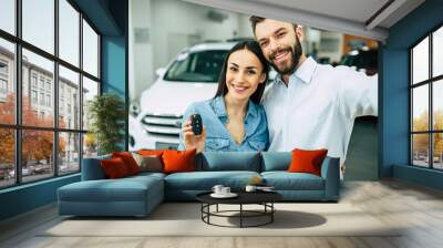 Happy young hugging couple chooses and buying a new car for the family in the dealership. Wall mural