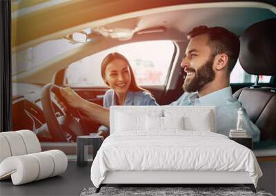 Happy young smiling couple riding in car on the road. Handsome bearded man is sitting at the wheel. Wall mural