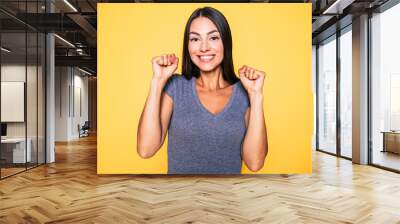 I'm so happy. Portrait of young excited attractive brunette woman in T-shirt with hands up and happy face isolated on yellow background Wall mural