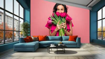 International Women's Day. Extremely happy woman in a bright pink dress is smelling a bunch of spring flowers, which she is holding in her hands. Wall mural