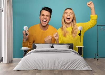 Joyful mood. Excited couple is posing on emerald background, wearing yellow sweaters and expressing happiness and victory with their poses, gestures and facial expressions. Wall mural