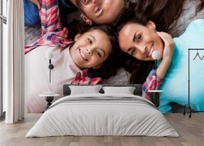 Lovely family. Close up photo of beautiful young family lying on the floor head to head, smiling broadly and hugging together. Wall mural