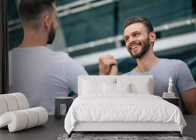 Men's friendly handshake. Two young bearded handsome friends in casual t-shirts are posing together on the city background. Wall mural