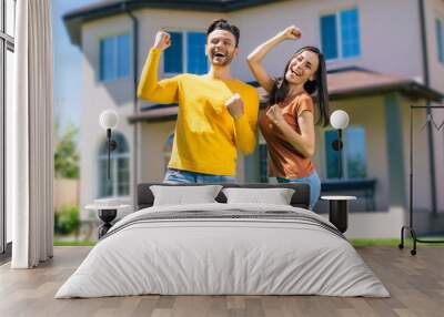 Modern beautiful excited young couple in love standing in front of the new big house with the keys in hands and hugging while they celebrating this buying Wall mural