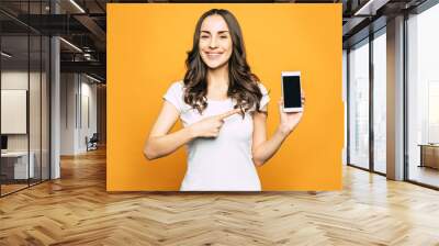 Note that. Glad pretty girl is pointing right on the phone in her hand with riant smile on her beautiful face in front of spice orange background. Wall mural