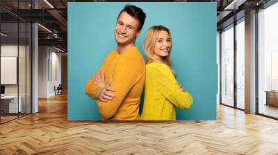 Partners in whole life. Handsome man and alluring girl are standing back to back, posing together in profile, looking in the camera and smiling sincerely. Wall mural