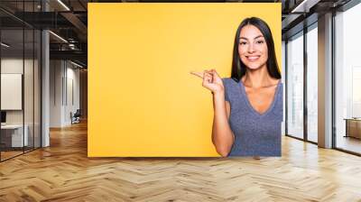 Photo of young excited beautiful happy brunette woman, girl pointing away and smile isolated on yellow background banner Wall mural