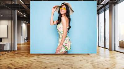 Portrait of cute summer brunette woman in hat, sunglasses and colorful dress, stylish girl have a fun and posing on blue background Wall mural