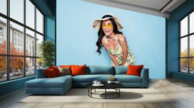 Portrait of cute summer brunette woman in hat, sunglasses and colorful dress, stylish girl have a fun and posing on blue background Wall mural