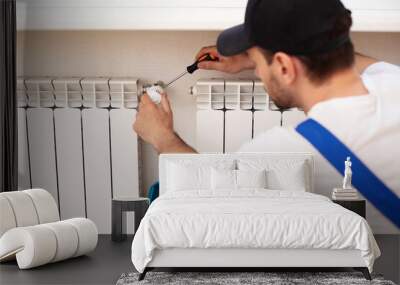 Professional young repairman in special uniform with tools is installing radiators and thermostat in domestic room Wall mural