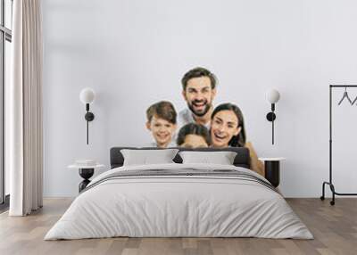 Relationship concept. Beautiful and happy smiling young family in white T-shirts are hugging and have a fun time together while sitting on the floor and looking on camera. Wall mural