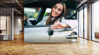 Smiling gorgeous young business woman holds the key in hand from her new car while testing this purchase Wall mural