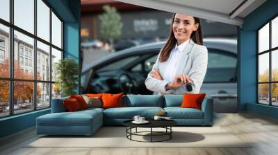 Smiling gorgeous young business woman holds the key in hand from her new car while testing this purchase Wall mural