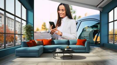 Successful smiling attractive woman in formal smart wear is using her smart phone while standing near modern car outdoors Wall mural