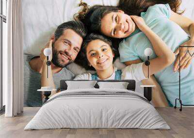 Top view photo of a beautiful happy family lying on the bed and have fun while they looking on camera Wall mural