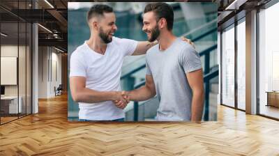 Two happy excited handsome bearded best friends in casual clothes are handshaking, hugging while standing outdoor. Wall mural