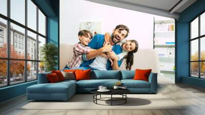 We are loving our father very much. Handsome dad playing with beautiful happy kids on the couch at home Wall mural