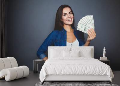 You can make purchases. Beautiful young woman in casual clothes joyfully holding in her hand a lot of dollars on a gray background isolated. The concept of money and banking. Wall mural