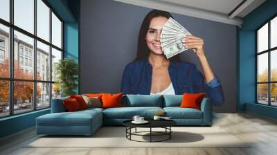 You can make purchases. Beautiful young woman in casual clothes joyfully holding in her hand a lot of dollars on a gray background isolated. The concept of money and banking. Wall mural