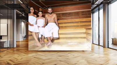 Young beautiful happy father and mother with little cute daughter in the bath towels are relaxing in the hot sauna Wall mural