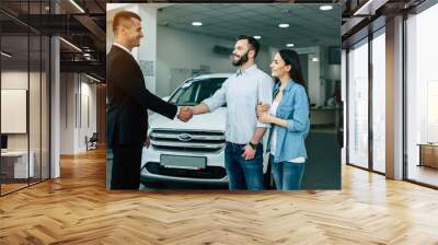 Young modern happy couple buying a new car in city dealership and talking with salesman Wall mural