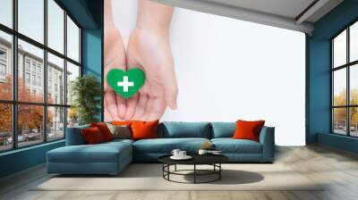 Hands holding a beautiful green heart with hospital white cross symbol on it showing a concept of Health care service, cancer treatment and heart surgery. Banner top view Isolated on white background. Wall mural