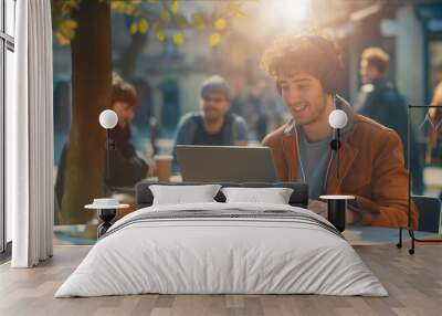 A man is seated at a table, engrossed in his laptop computer at a cafe. Wall mural