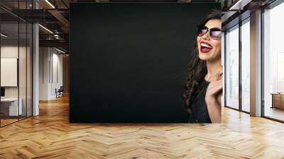 Overjoyed young woman in sunglasses holding shopping bags on shoulder isolated over black background Wall mural