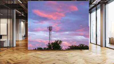 A silhouette of a cell tower stands tall against a vibrant sunset sky, its antennas reaching into the colorful horizon. The contrast of technology and nature highlights modern connectivity moment. Wall mural