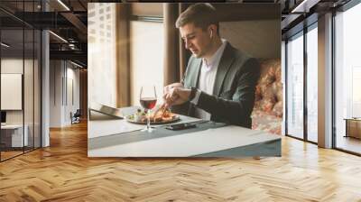 A young and attractive man uses his tablet while eating Traditional English breakfast. Sausage, beans, eggs, bread and salad in an indoor restaurant. Wall mural