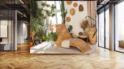 New furniture in cozy living room. Modern interior design in boho apartment. bamboo armchair and plants in room, straw hats on white wall. Wall mural