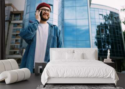 Successful modern handsome bearded hipster man talking over the smartphone, smiling and looking to the side. Wall mural