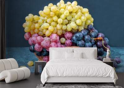 Yellow, black and red grapes in a wicker basket on a table. Wall mural